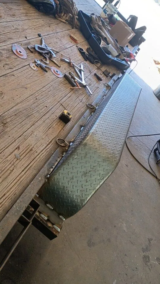 Diamond-plate fender and welded D-ring tie-downs along a wood-deck flatbed trailer
