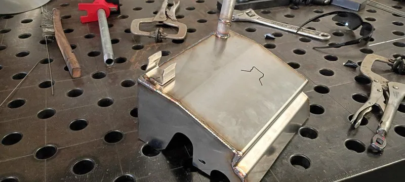 Fabricated stainless steel enclosure with a welded tube on top, on a fixture welding table