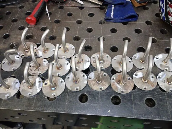 Row of fabricated stainless steel hooks welded to round base plates on the welding table