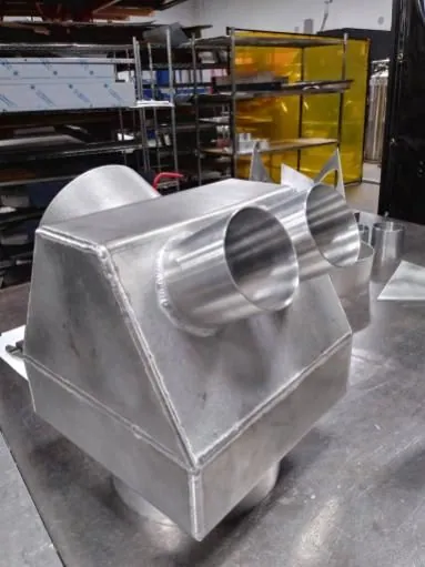 Fabricated stainless steel housing with two round pipe outlets on a square base