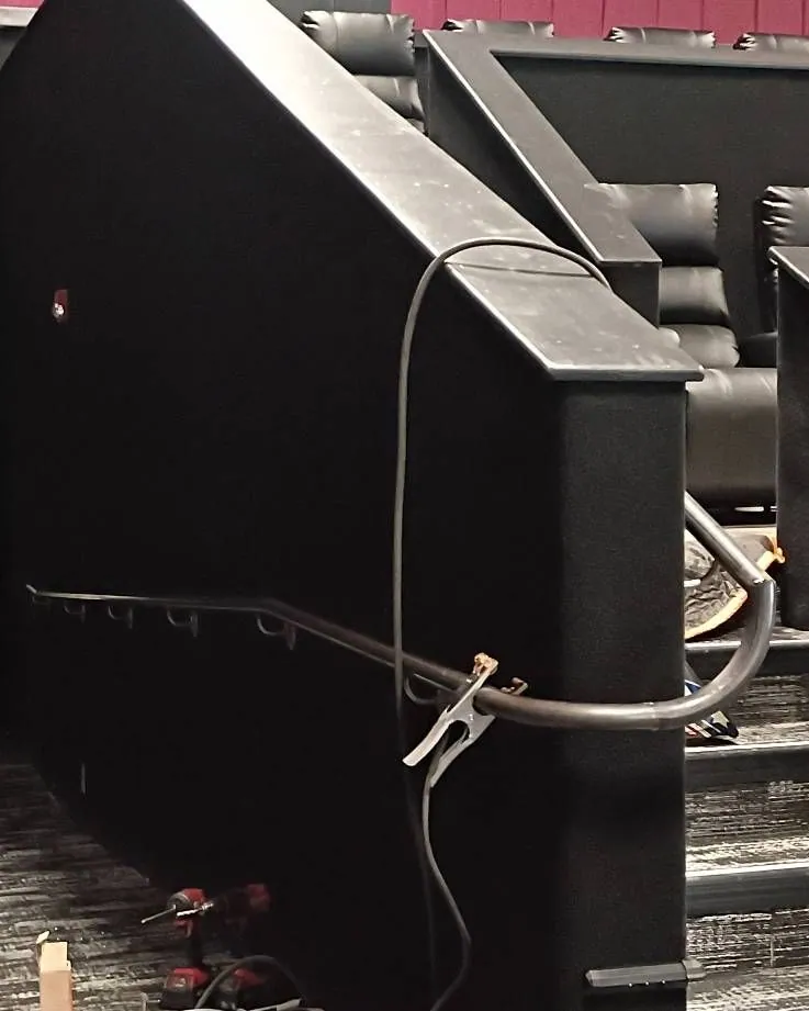 Metal handrail being installed along a movie theater staircase, clamps still in place