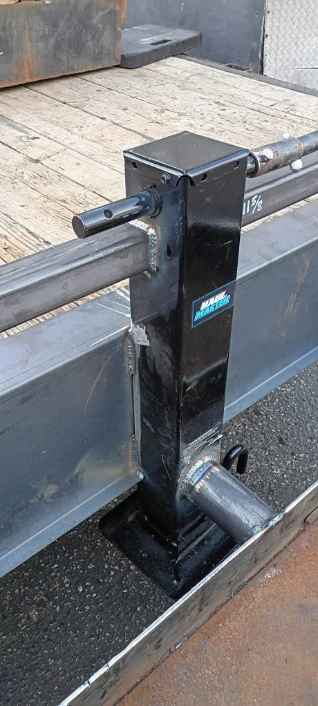 Black square trailer jack welded onto a flatbed trailer frame