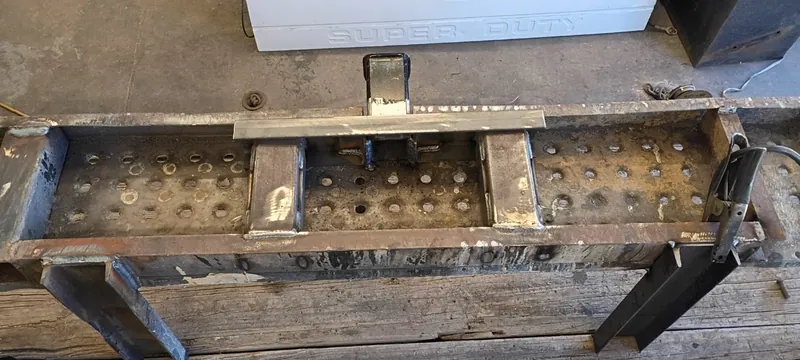 Custom steel step bumper with perforated step plates and a center hitch receiver, mid-build in the shop