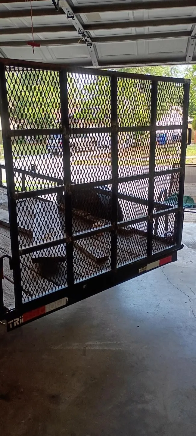 Steel utility trailer with an expanded-metal mesh ramp gate, parked in a garage