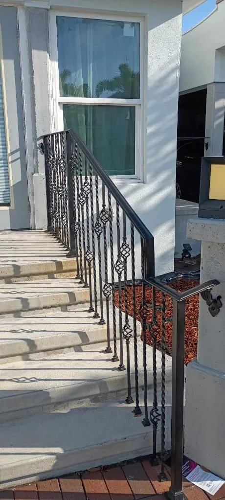 Ornate black wrought-iron handrail along concrete steps to a front door